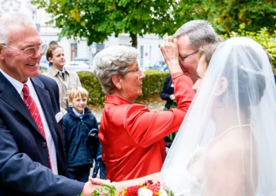 Hochzeitsfoto in München-Lehel: Braut empfängt Glückwünsche von Gästen im Freien, mit Hochzeitsreportage-Stimmung.
