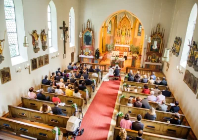 Hochzeitsfoto einer kirchlichen Trauung in einer Kirche in München Pasing mit Gästen und Brautpaar am Altar.