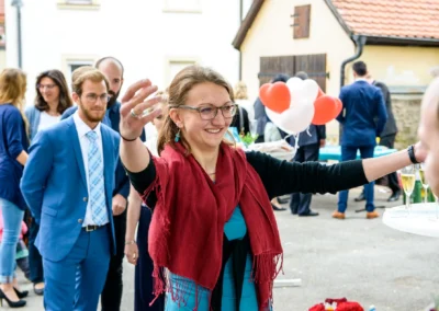 Hochzeitsreportage in Ansbach: Frau in rotem Schal lacht und streckt die Arme aus, umgeben von Hochzeitsgaesten.