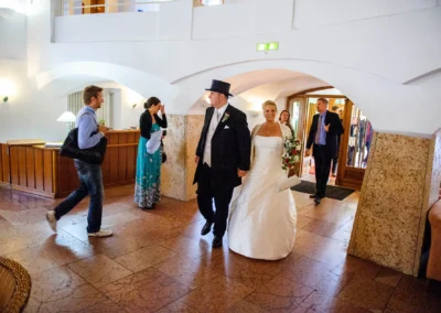Brautpaar betritt Hochzeitsempfang im Bayerischen Hof Miesbach, sie laecheln und sind von Gaesten umgeben.