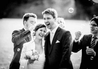 Brautpaar lacht mit Freunden und Seifenblasen bei einer Hochzeitsreportage im englischen Garten Muenchen.