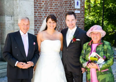 Gruppenfoto bei einer Hochzeit in Gauting nahe Muenchen mit Braut, Braeutigam und Gaesten vor Backsteinmauer.