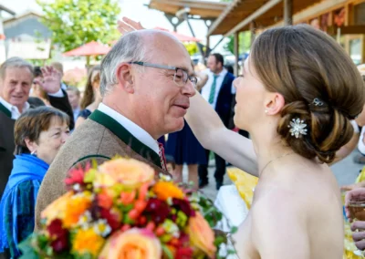 Hochzeitsreportage nahe Rosenheim: Braut in weissem Kleid umarmt Gast, Blumenstrauss im Vordergrund.