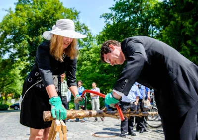 Zwei Personen saegen gemeinsam einen Baumstamm bei einer Hochzeitsfeier in Schloss Ismaning, Hochzeitsreportage.