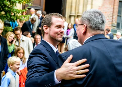 Ein Mann gratuliert dem Braeutigam bei einer Hochzeitsfeier in Muenchen-Lehel. Gaeste im Hintergrund.