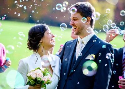 Brautpaar lacht umgeben von Seifenblasen im Englischen Garten in Muenchen, Hochzeitsfoto bei einer Trauung.