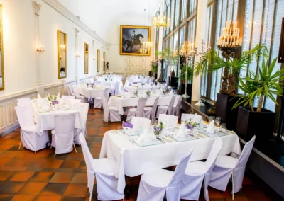 Elegantes Hochzeitsfoto: Festlich gedeckte Tische im Palmenhaus Schloss Nymphenburg, Kerzenleuchter und Palmen.
