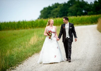 Brautpaarfoto auf ländlichem Weg im Dachauer Hinterland, die Braut hält einen Blumenstrauss, Hochzeitsfotografie.