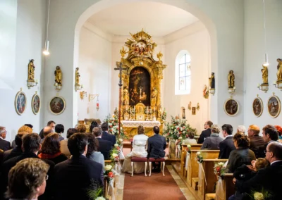 Kirchliche Trauung am Starnberger See, Brautpaar sitzt vor Altar, Gaeste in Kirche. Hochzeitsreportage München.