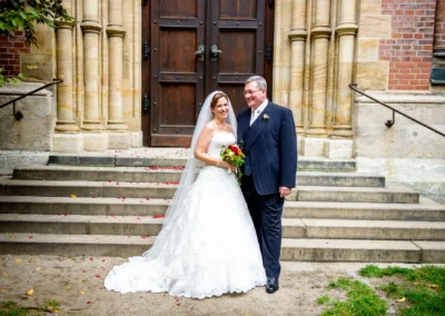 Brautpaar vor Kirche in muenchen-lehel mit Blumenstrauss und Hochzeitskleid. Aufnahme bei einer Hochzeit.