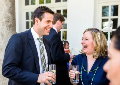 Lachendes Paar mit Getränken auf einer Hochzeit im Kurhaus Bad Toelz, festgehalten in der Hochzeitsreportage.