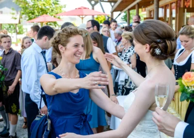 Braut in weissem Kleid umarmt Gast in Blau bei einer Hochzeit nahe Rosenheim, festgehalten vom Hochzeitsfotograf.