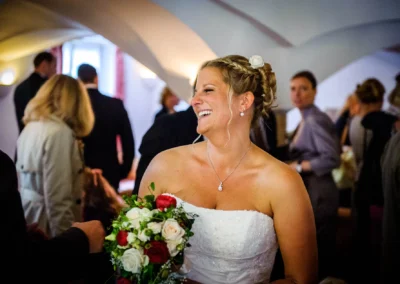 Braut lacht mit Blumenstrauss in festlicher Umgebung in Miesbach. Hochzeitsfotografie bei einer Hochzeit.