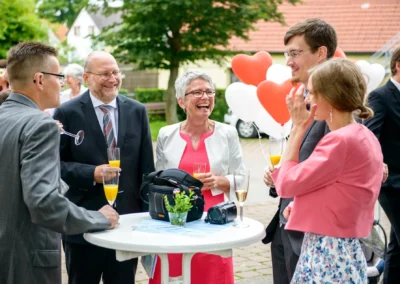 Gruppe lachender Hochzeitsgaeste bei Empfang in Ansbach mit Herzluftballons und Getraenken. Hochzeitsfotograf aus Muenchen.