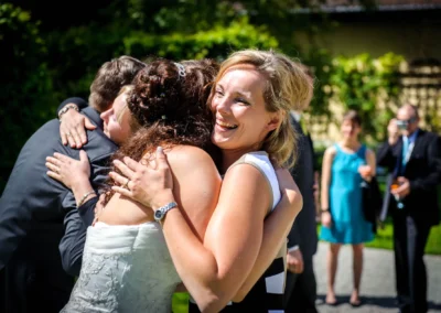 Braut und Gast lachen und umarmen sich auf einer Hochzeit im Schloss Aufhausen nahe Muenchen im Sonnenschein.