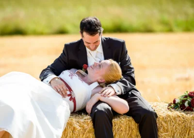Brautpaar auf Heuballen, romantisches Hochzeitsfoto im Dachauer Hinterland, Brautstrauss mit roten Rosen.