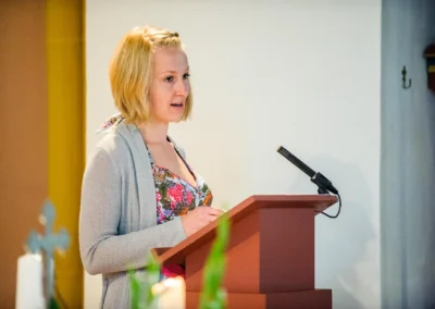 Frau haelt Rede waehrend kirchlicher Hochzeit in Muenchen mit Mikrofon. Hochzeitsfotografie in Pasinger Stadtpark.