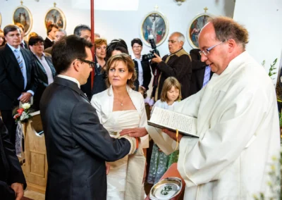 Brautpaar bei kirchlicher Trauung am Starnberger See, Priester spricht Gebet, umgeben von Hochzeitsgaesten.