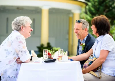 Drei Personen lachen bei einer Hochzeit am Tisch im Kurhaus Bad Toelz, festgehalten von einem Hochzeitsfotografen.