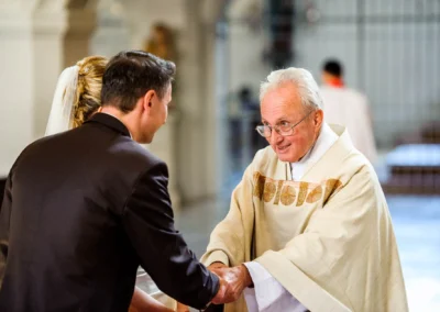 Priester bei kirchlicher Trauung in Sankt Sylvester Muenchen haelt Haende des Brautpaars, Hochzeitsfotografie.