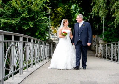 Brautpaar geht Hand in Hand über eine Brücke in München, Hochzeitsfotografie im Grünen.