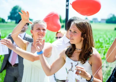 Gäste bei Hochzeit nördlich von Dachau lassen rote Herzluftballons steigen, Hochzeitsfoto von Hochzeitsreportage.