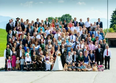 Großes Gruppenfoto bei Hochzeit nahe Rosenheim. Die Gäste stehen lächelnd in festlicher Kleidung. Hochzeitsfoto.