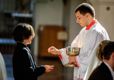 Kleriker reicht Hostie waehrend der kirchlichen Trauung in Sankt Sylvester Muenchen. Hochzeitsreportage in Schwabing.