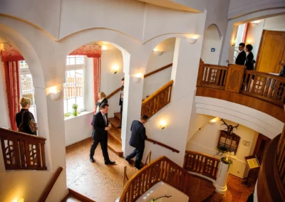Gäste in eleganter Kleidung betreten bei einer Hochzeit ein Treppenhaus im Bayerischen Hof Miesbach. Hochzeitsreportage.