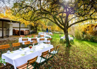 Gedeckte Tische im Garten bei Hochzeit in Gruenwald, umgeben von herbstlichem Laub und Baumen. Hochzeitsreportage.