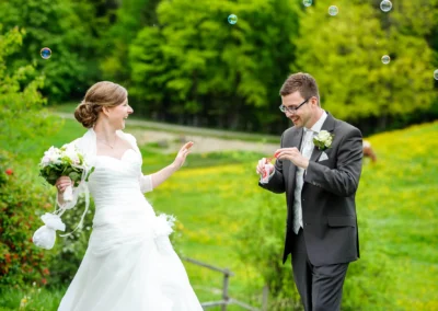 Brautpaar mit Seifenblasen bei Hochzeitsportraits im Aschbacher Hof, beide lachen herzlich, farbenfrohe Naturkulisse.