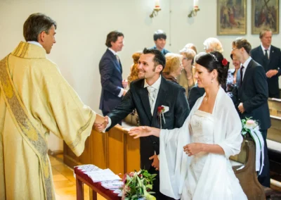 Brautpaar waehrend der kirchlichen Trauung in München, Hochzeitsfoto zeigt Brautpaar und Priester im Dialog.