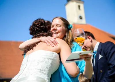 Frau in Blau umarmt Braut mit weissem Kleid, Hintergrund Schloss Aufhausen bei Erding, Hochzeitsfotografie.