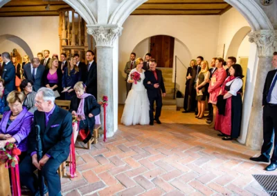 Braut schreitet zur Trauung in Landshut, begleitet von Gaesten in einer Kirche, Hochzeitsreportage von Burg Trausnitz.