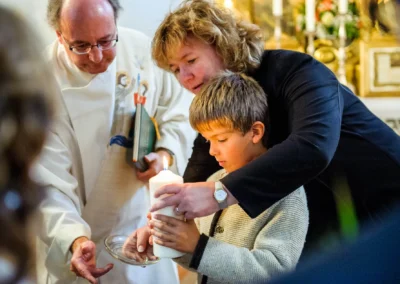 Ein Junge zündet eine Kerze an, unterstützt von einem Erwachsenen, in einer Kirche bei der Hochzeit südlich von München.