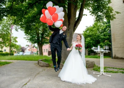 Brautpaar vor Baeumen mit Herzballons und Blumenstrauss bei Hochzeit in Ansbach, Hochzeitsfotografie im Freien.