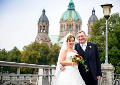 Brautpaar lacht bei Hochzeitsreportage in München-Lehel, Kirche im Hintergrund. Hochzeitsfoto in idyllischer Kulisse.