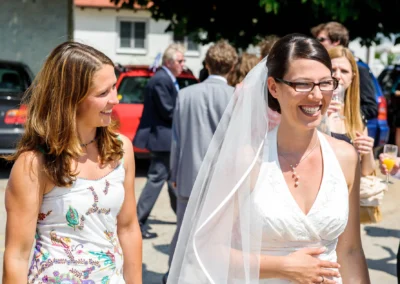 Braut in weissem Kleid laechelt neben Freundin bei Hochzeitsreportage nordlich von Dachau.