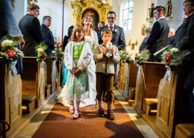 Brautpaar und Kinder schreiten waehrend der kirchlichen Trauung zur Hochzeitsfotografie in Harkirchen.