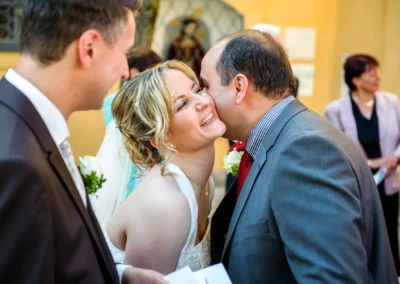 Braut lacht und wird von einem Gast auf der Wange gekuesst bei Hochzeit in Schwabing, Muenchen. Hochzeitsfoto.
