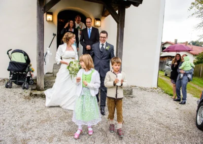 Brautpaar verlaesst Kirche mit Blumenkindern bei Hochzeit am Starnberger See, festgehalten in stilvoller Hochzeitsfotografie.