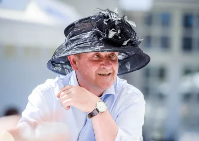 Mann mit schwarzem Hut bei einer Hochzeitsfeier im Kurhaus Bad Toelz in der Sonne lächelnd.