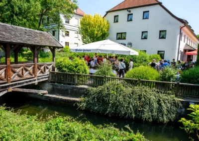 Gartenfest bei Hochzeit in Gasthof zur Mühle Ismaning, mit Gästen unter einem weißen Sonnenschirm. Hochzeitsfotograf.