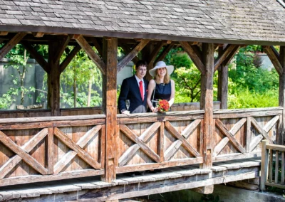 Paar auf Holzbrücke bei Hochzeit in Ismaning, Hochzeitsfoto mit Blumenstrauß und Sektgläsern.
