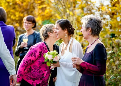 Braut lacht mit Freundinnen bei einer Hochzeit im Garten des Alten Wirts Gruenwald. Hochzeitsfotografie im Herbst.