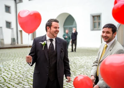 Zwei Männer halten rote Herzballons bei einer Hochzeit im Schloss Höchstädt an der Donau. Hochzeitsreportage.