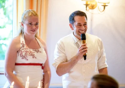 Braut und Bräutigam bei der Hochzeitsfeier in Röhrmoos, Bräutigam hält Mikrofon. Hochzeitsfotografie im Dachauer Hinterland.