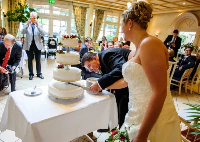 Brautpaar schneidet Hochzeitstorte in Miesbach an. Gaeste im Hintergrund, Hochzeitsfotografie im Bayerischen Hof Miesbach.
