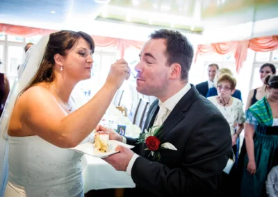Brautpaar bei der Hochzeit in Wessling, Braut fuettert Braeutigam Kuchen. Hochzeitsfotografie im Landkreis Starnberg.