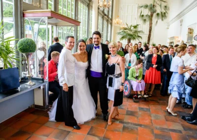 Hochzeitsfoto im Palmenhaus Schloss Nymphenburg mit Brautpaar und Gästen, freundliche Stimmung bei der Hochzeit.